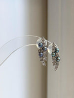 Iridescent freshwater pearls nestled among clear stones in a curved leaf design.