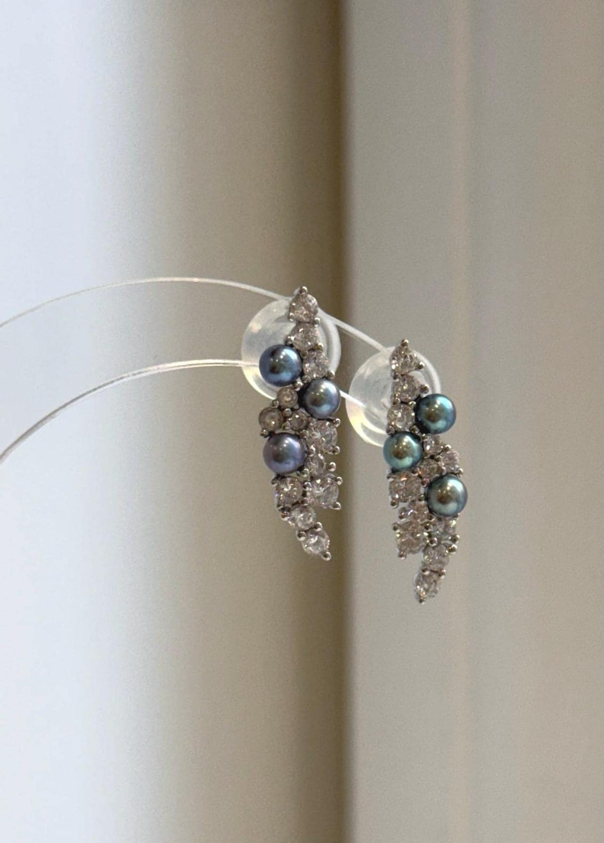 Pair of freshwater pearl leaf earrings displayed on a clear stand.