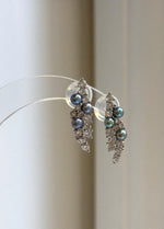 Pair of freshwater pearl leaf earrings displayed on a clear stand.