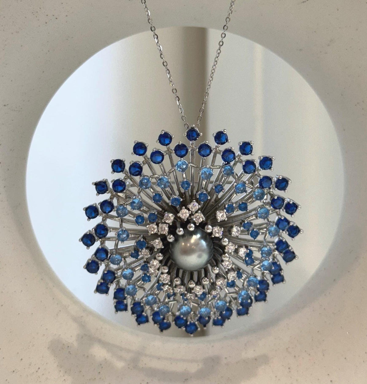 Round Tahitian pearl surrounded by radiating silver-tone branches and blue stones.