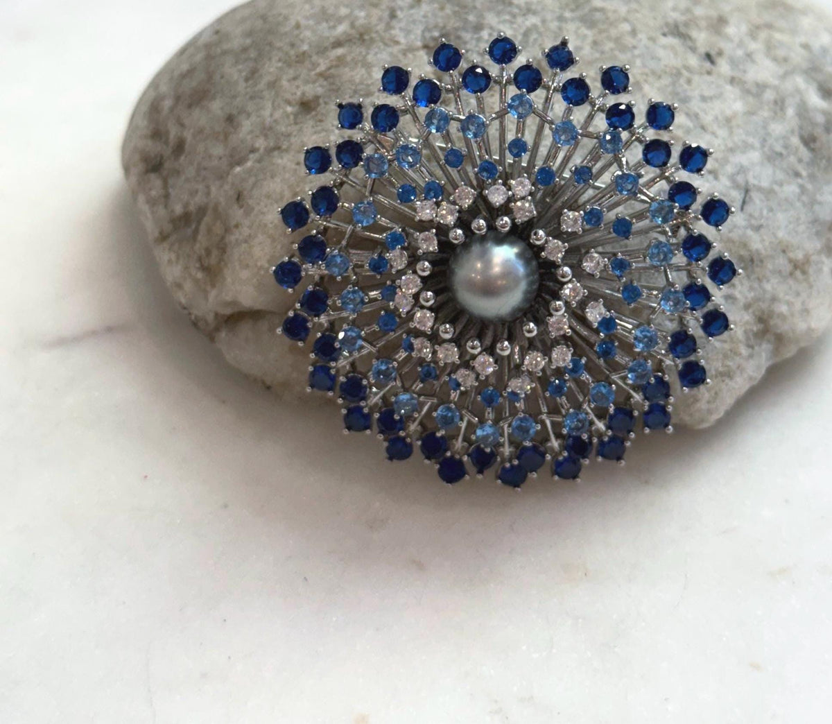 Lustrous platinum gray pearl at the center of a circular blue stone design.
