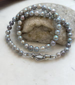 Saltwater pearl necklace beside a handwritten label, driftwood and a stone.