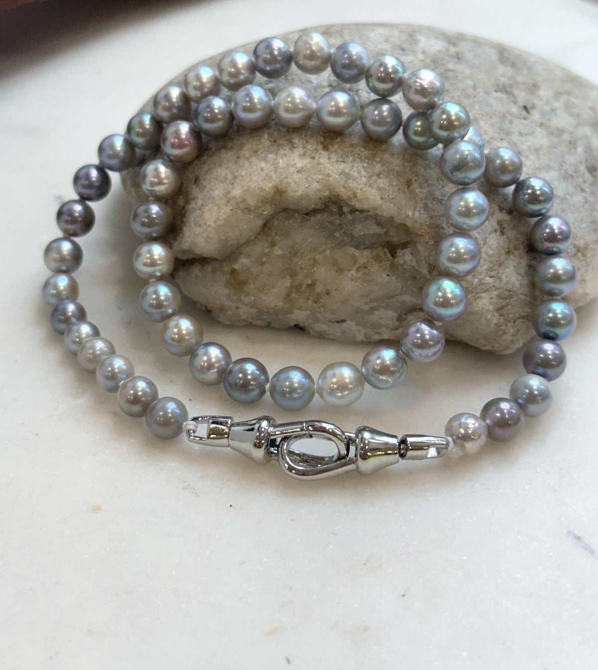 Saltwater pearl necklace beside a handwritten label, driftwood and a stone.