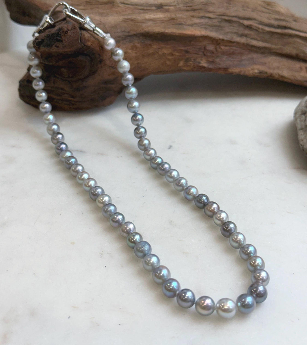 Blue grey saltwater pearl necklace displayed beneath rustic driftwood.