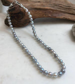 Blue grey saltwater pearl necklace displayed beneath rustic driftwood.