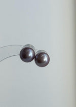 Lavender pearl necklace draped over a stone beside matching studs.