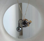 Dark metallic fish pendant with gold-tone fins and a dangling pearl.