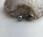 Reflective gray pearl suspended in front of an anglerfish pendant.