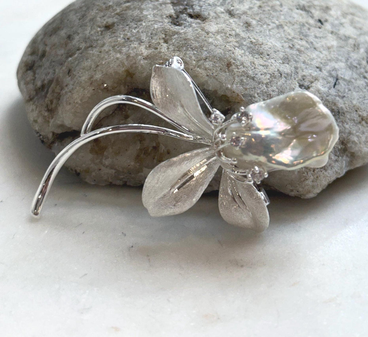 Iridescent baroque pearl above textured petals and curved stems.