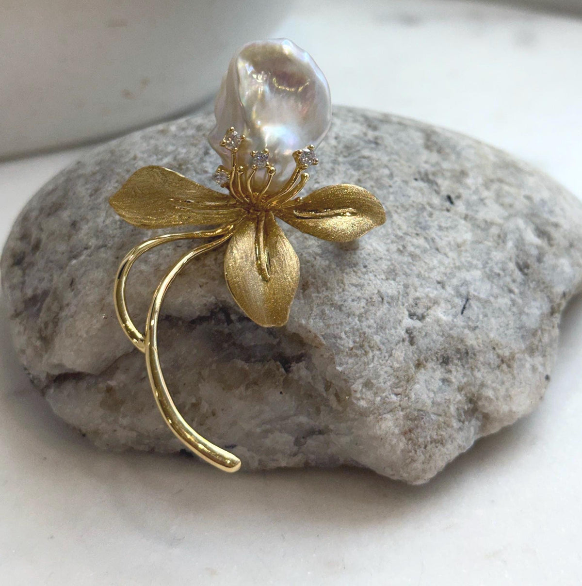 White baroque freshwater pearl floral brooch with textured gold-tone petals.