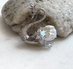 White pearl swan pendant displayed against a textured natural stone.