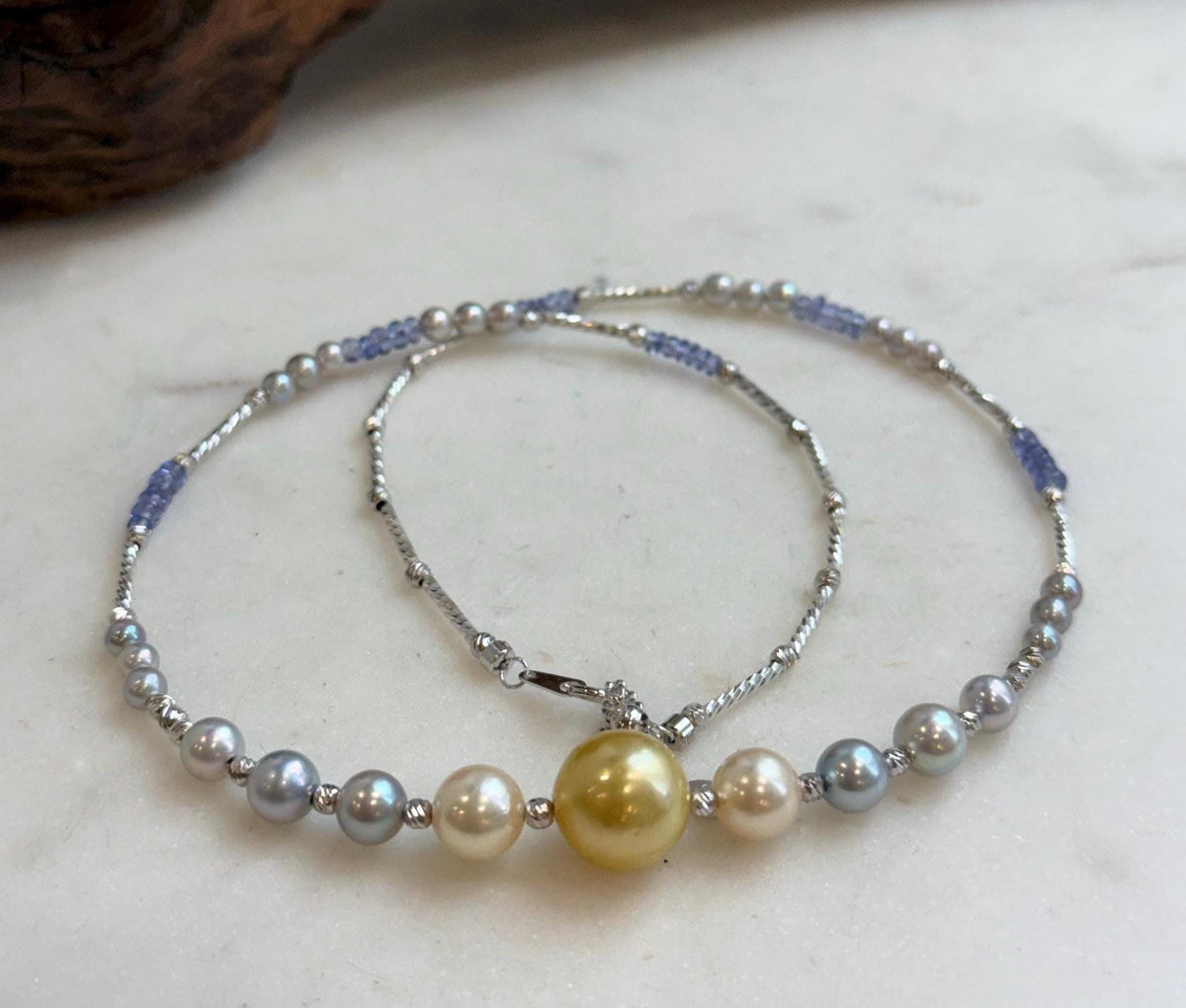 Multicolor pearl and tanzanite necklace arranged on a pale stone surface.