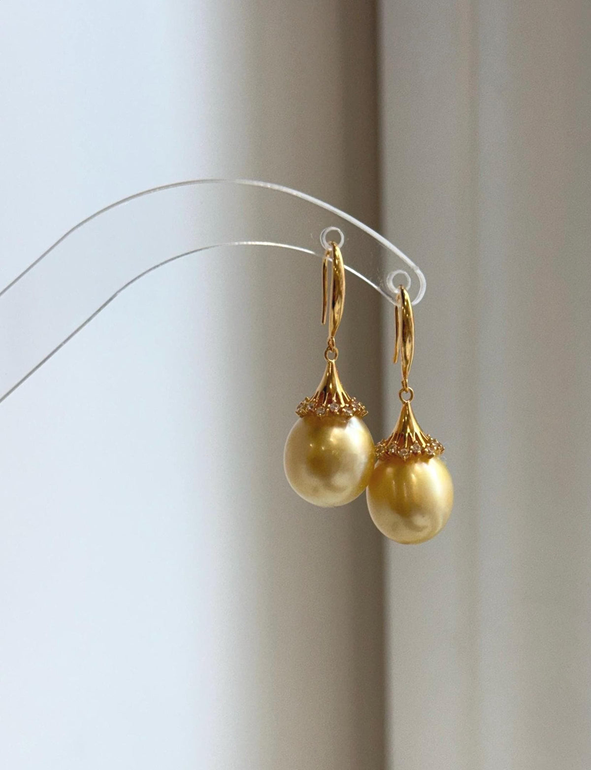 Golden South Sea pearl earrings resting on a pale marble surface beside a handwritten label.