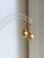 Golden South Sea pearl earrings resting on a pale marble surface beside a handwritten label.