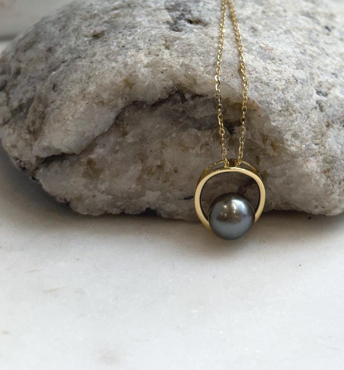 Taupe platinum pearl necklace displayed on a white sculptural jewelry stand.