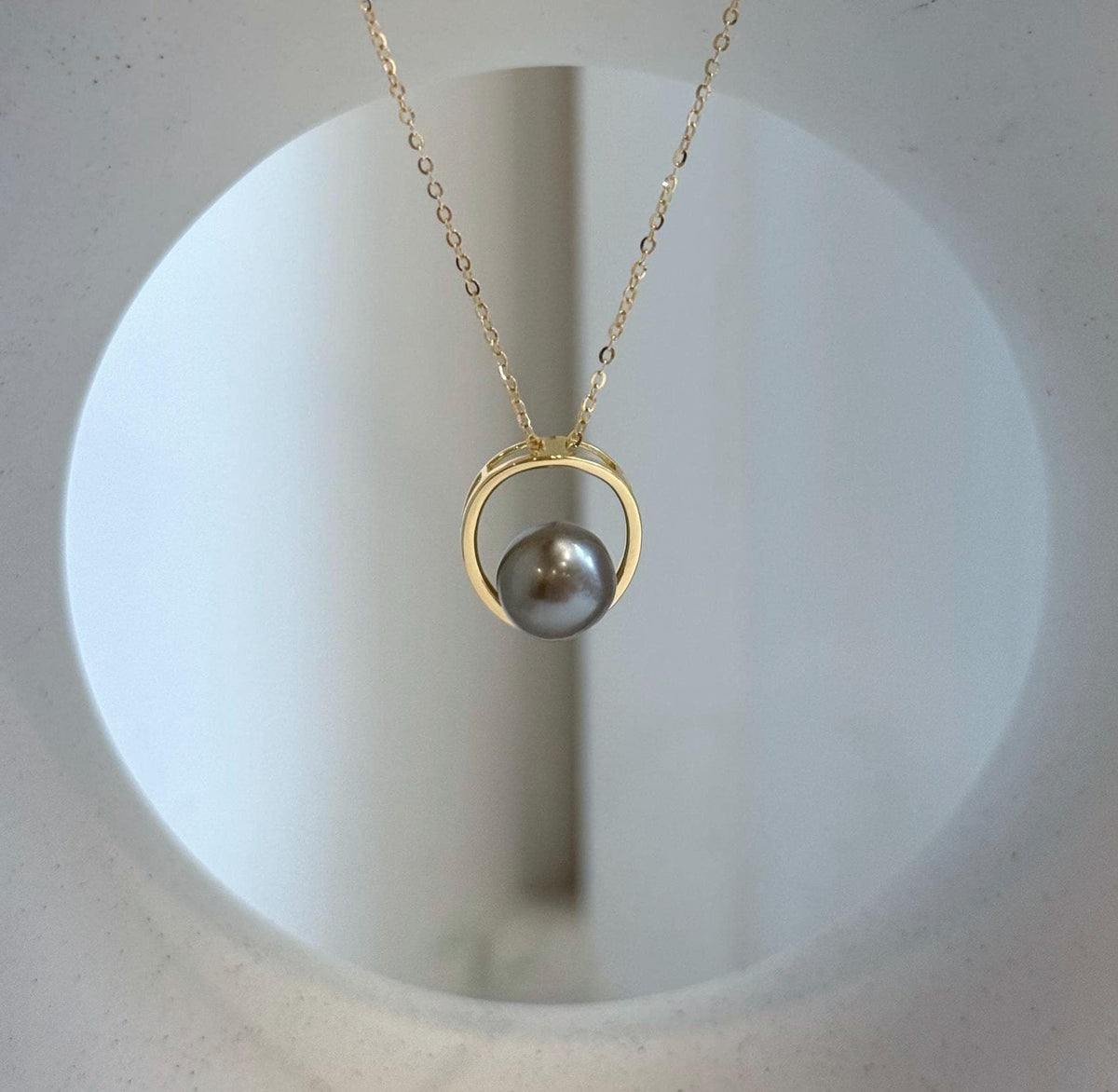 Reflective taupe pearl framed by a polished gold-tone circular setting.