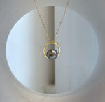 Reflective taupe pearl framed by a polished gold-tone circular setting.