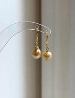 Champagne gold pearl earrings displayed on a clear acrylic stand.