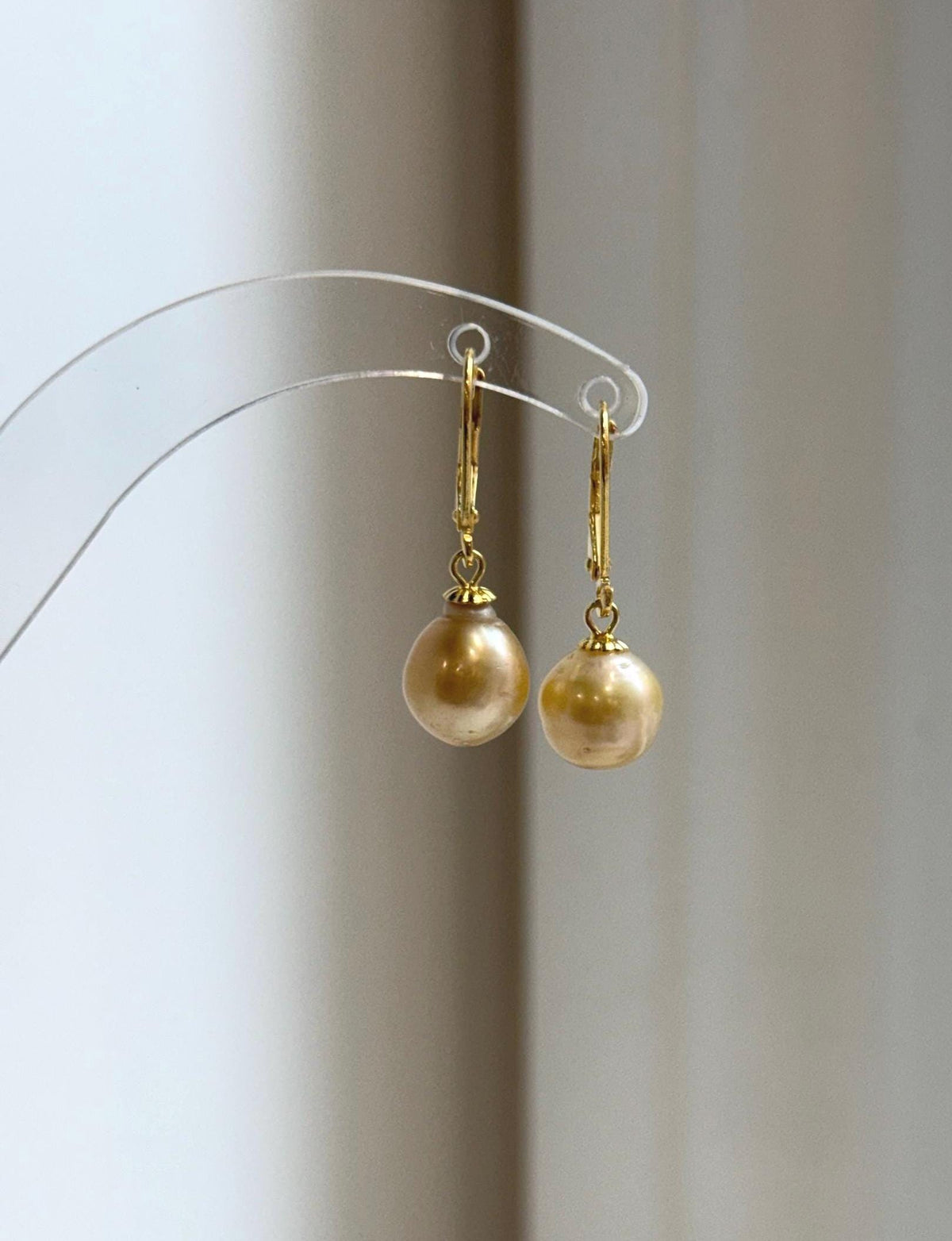 Champagne gold pearl earrings displayed on a clear acrylic stand.