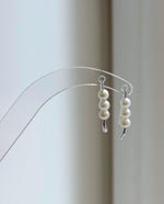 White pearl earrings displayed on a clear acrylic stand in natural light.