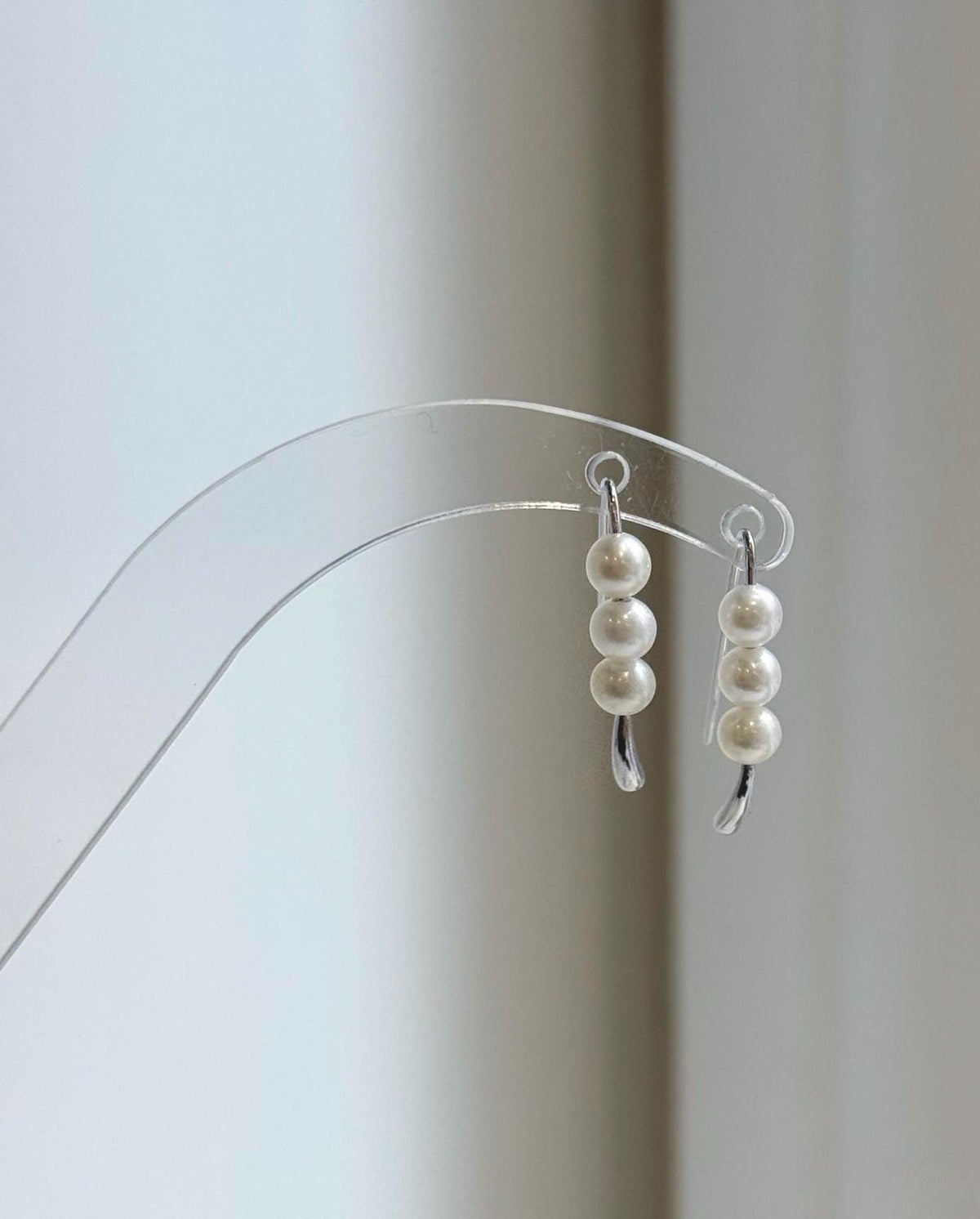 White pearl earrings displayed on a clear acrylic stand in natural light.