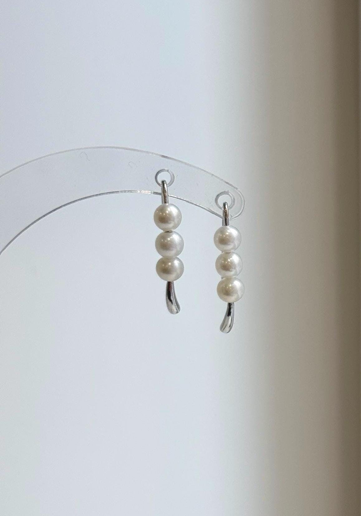 Curved sterling silver earrings featuring a row of three rounded white pearls.