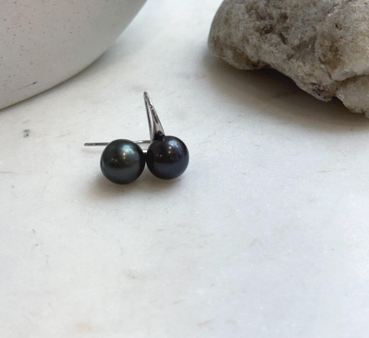 Lustrous hunter green pearls suspended from sleek silver ear hooks.