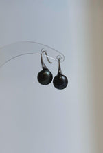 Pair of black-green pearl earrings displayed against a neutral background.