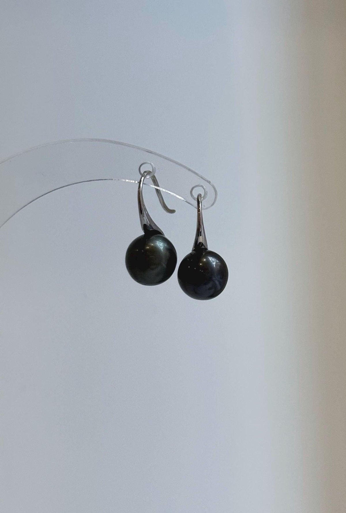 Pair of black-green pearl earrings displayed against a neutral background.