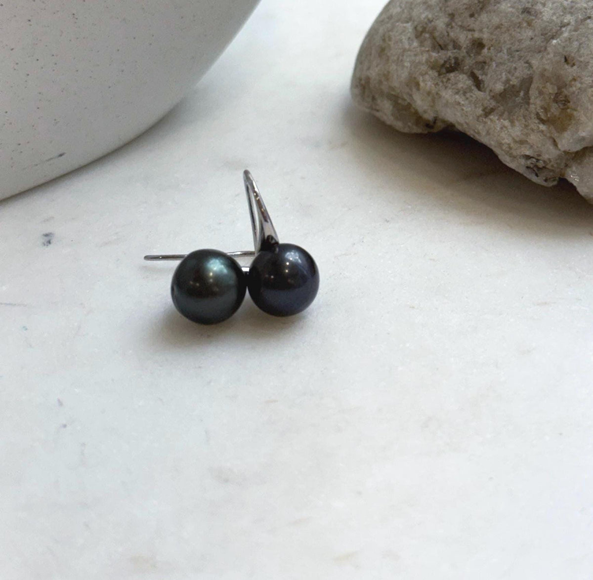 Black hunter green pearl earrings resting on a pale stone surface.