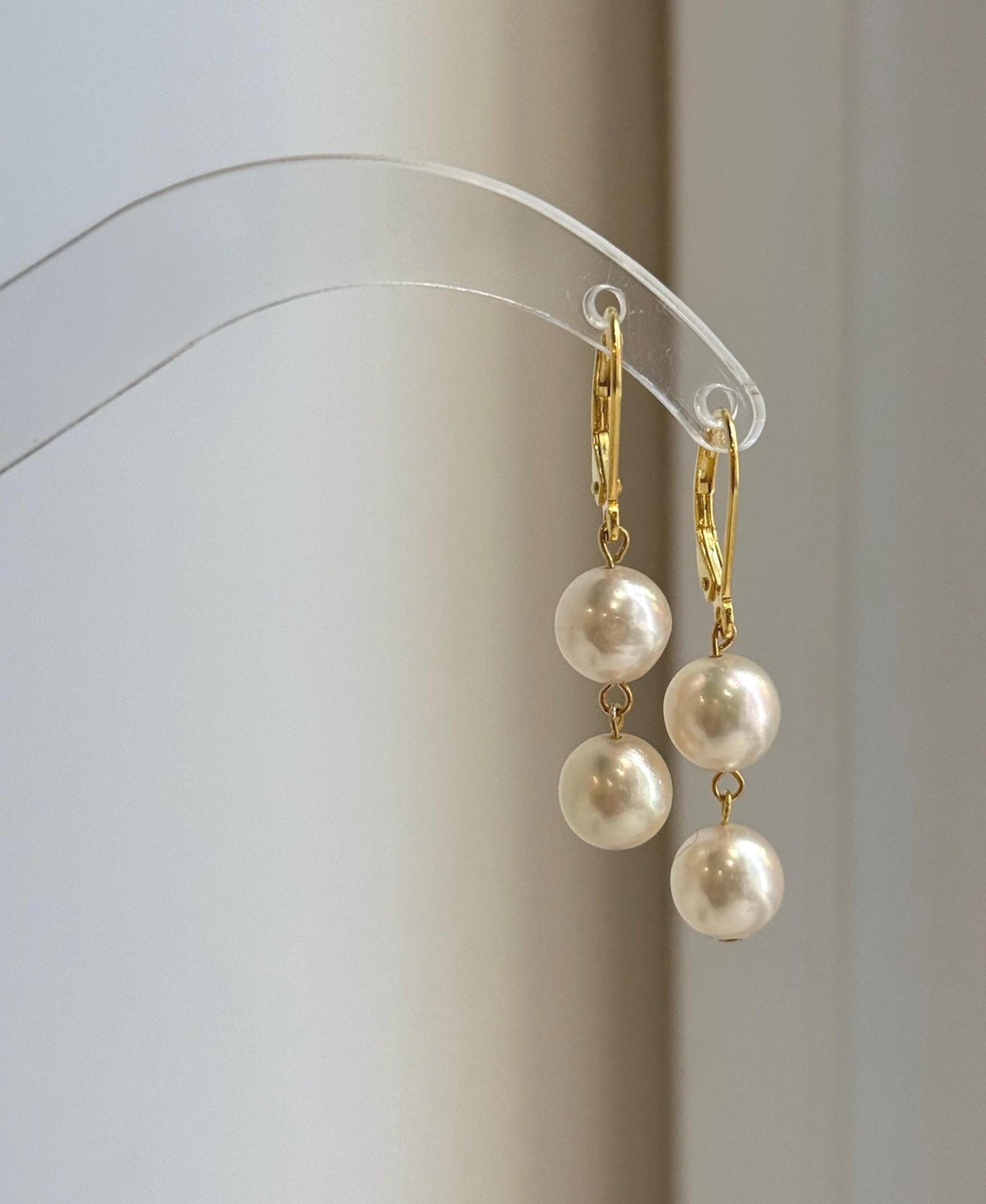 Ivory Akoya ocean pearl earrings hanging from a clear curved display stand.