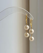 Ivory Akoya ocean pearl earrings hanging from a clear curved display stand.