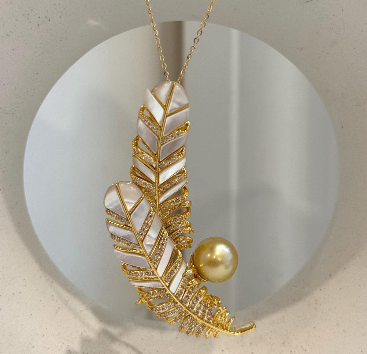 Golden pearl feather pendant displayed on a chain