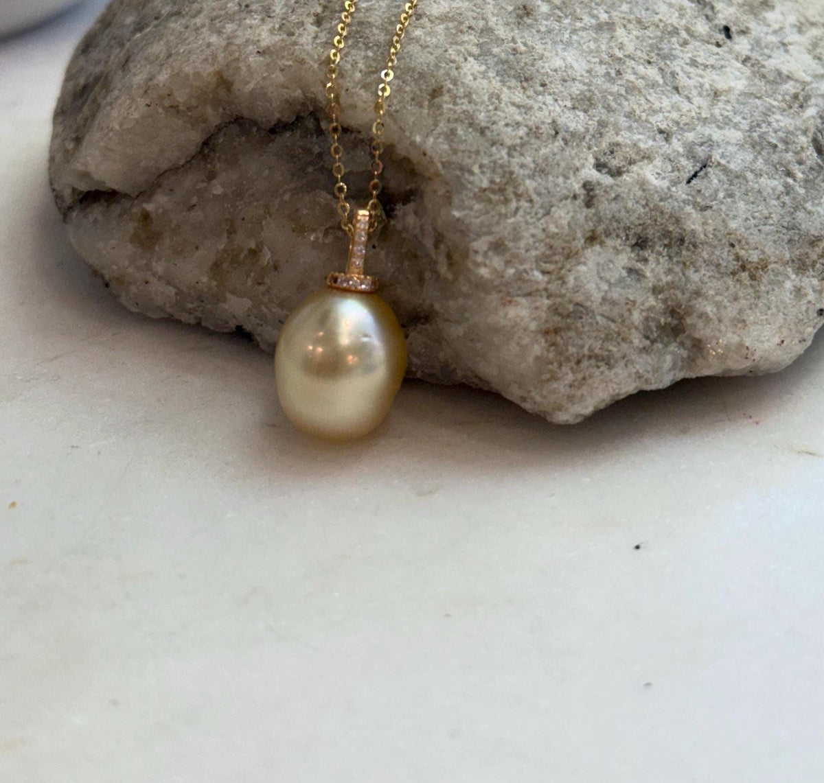 Golden pearl drop pendant displaying mirror luster and subtle color overtones.