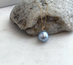 Silver blue ocean pearl pendant with a reflective surface and moissanite detailing in solid gold.