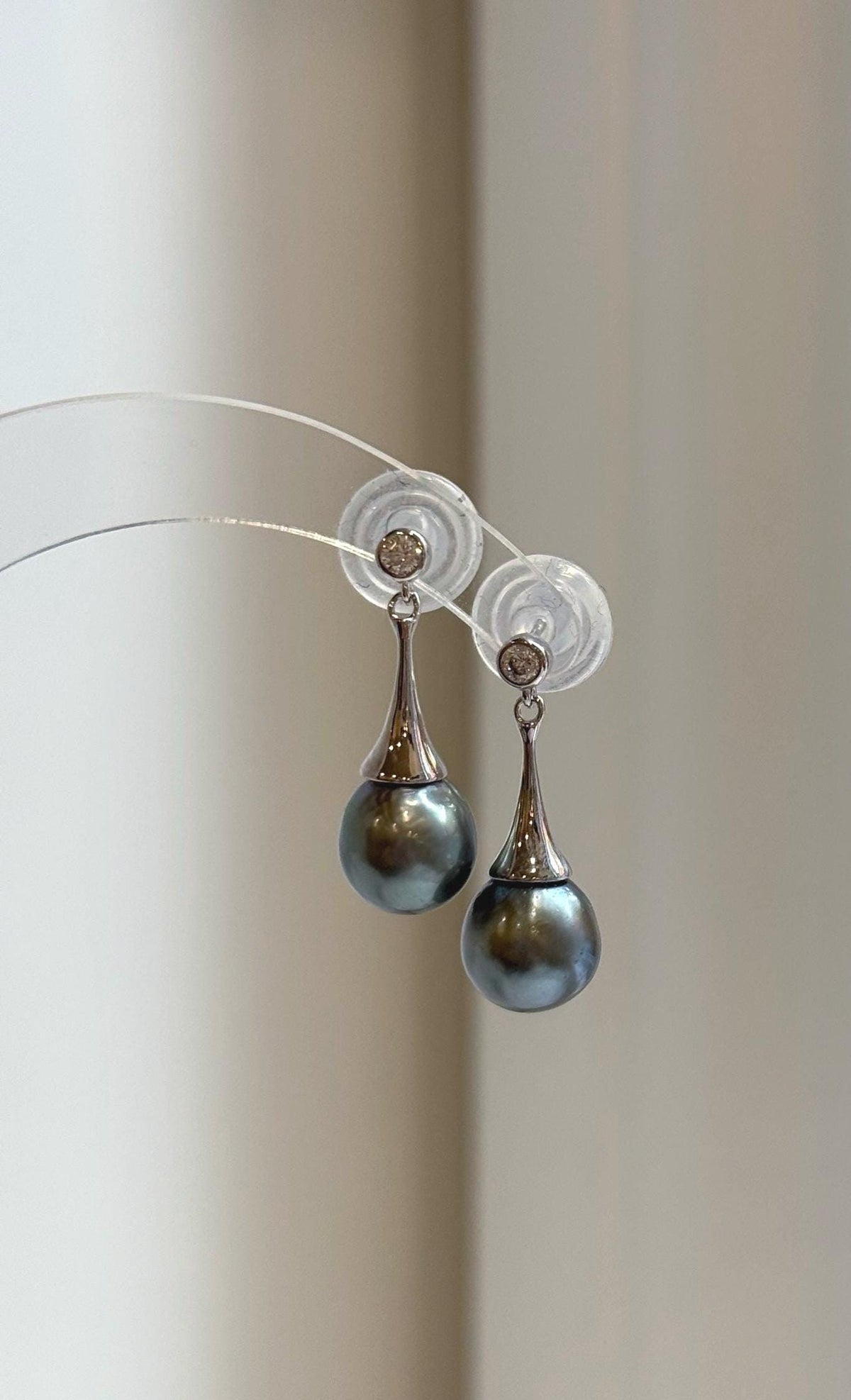 Dark gray pearl earrings displayed on a clear stand