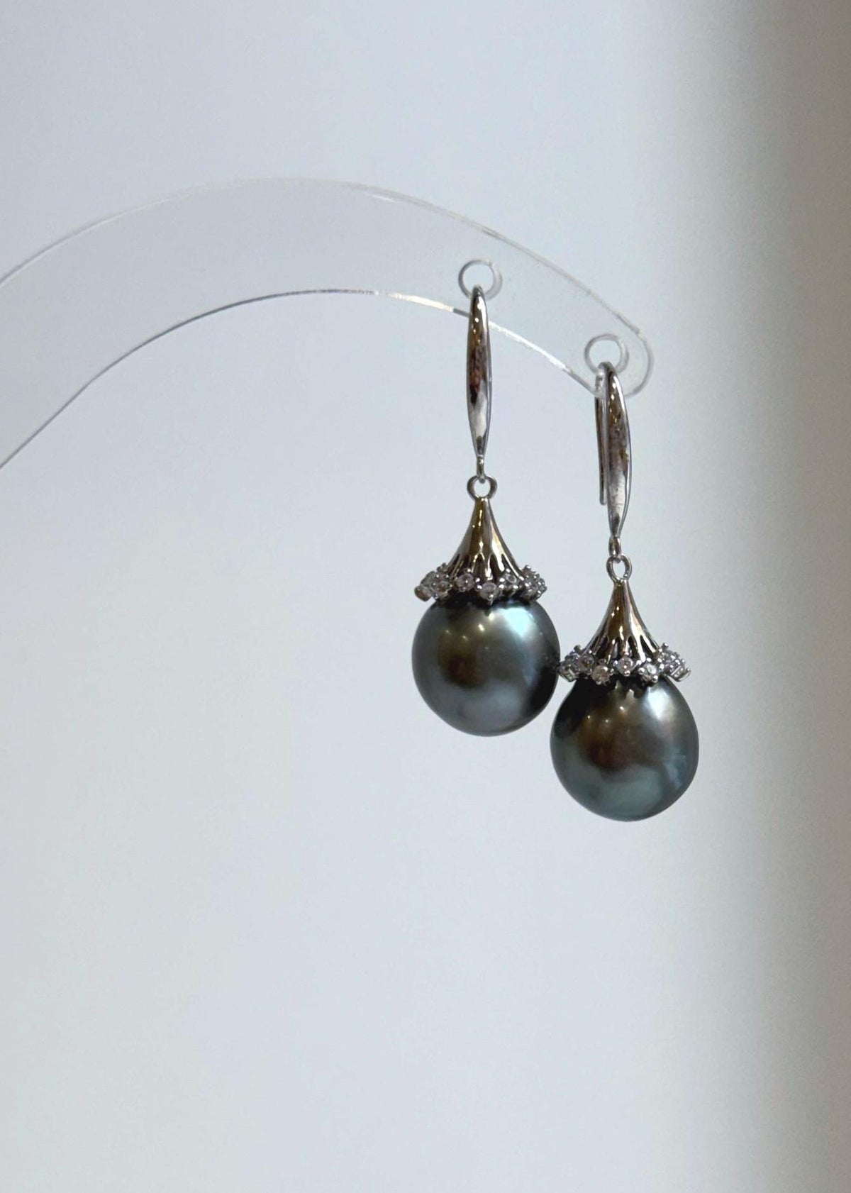 Silver floral pearl earrings on a clear display stand