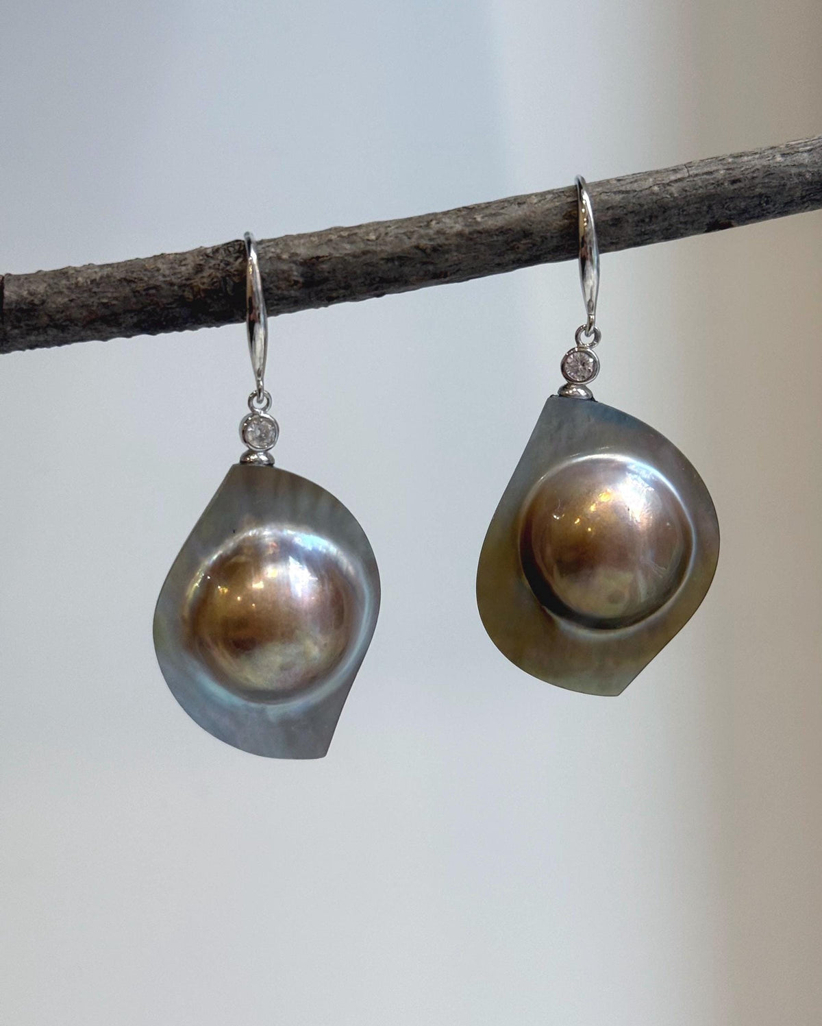 Golden pearl drop earrings displaying colorful iridescent overtones.