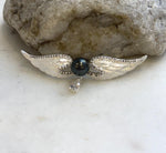 Hunter green pearl angel wing brooch displayed on a pale stone surface.