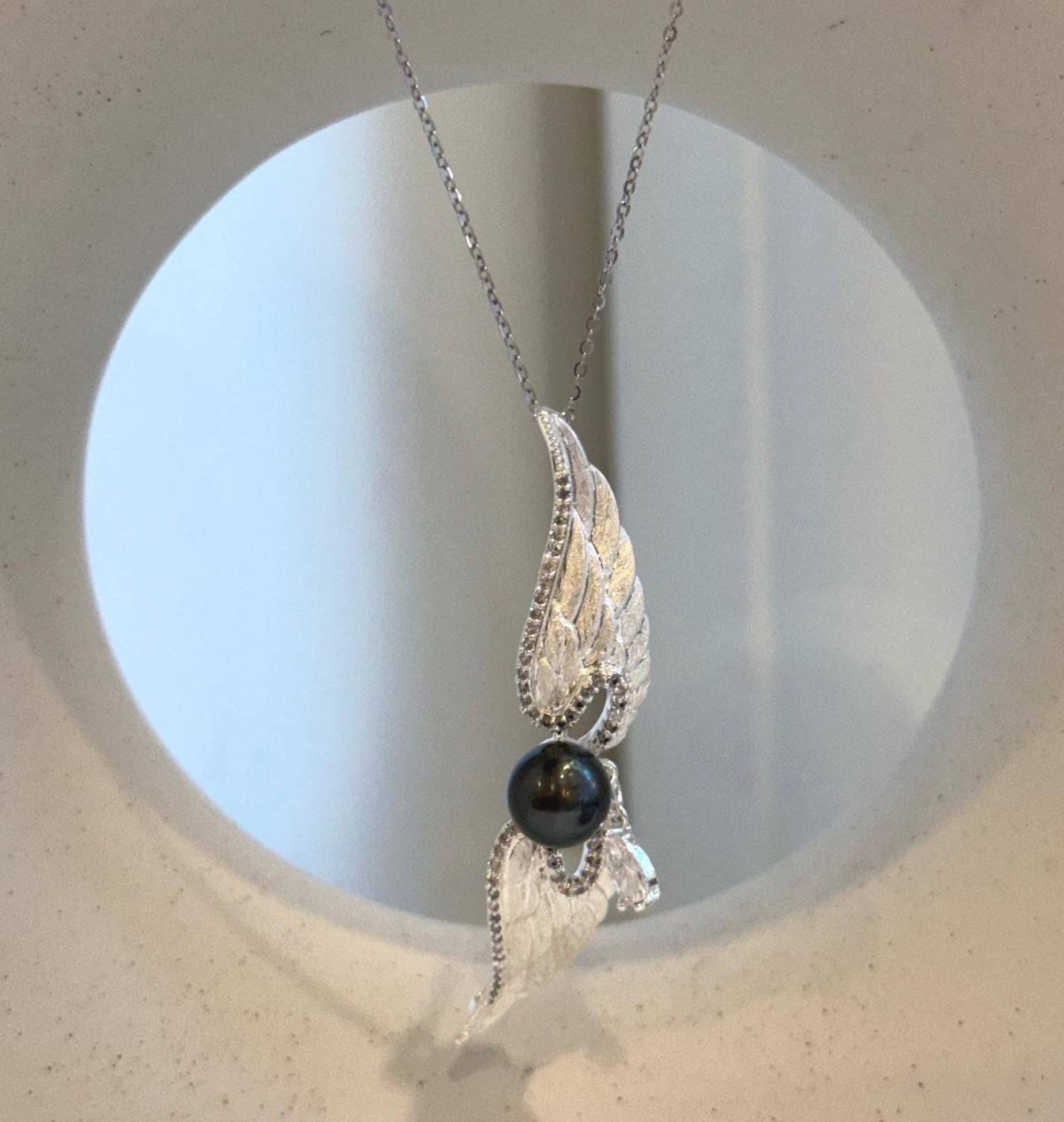 Wing-shaped pearl brooch pendant with a clear accent suspended beneath the central pearl.