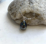 Tahitian teardrop pearl hanging beneath a silver knot, shown against a cream display.