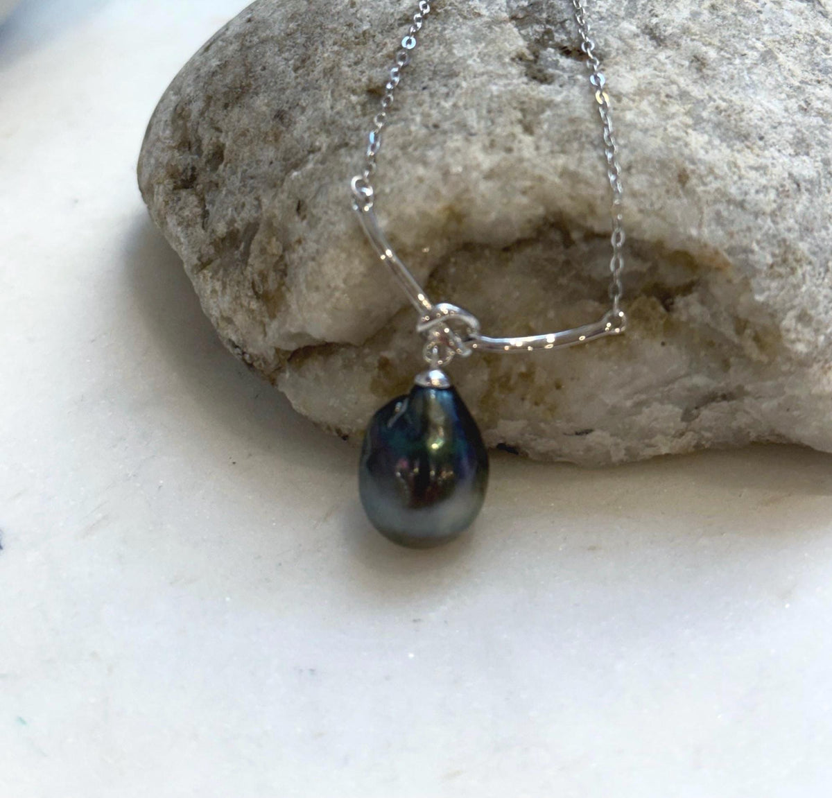 Tahitian teardrop pearl hanging beneath a silver knot, shown against a cream display.