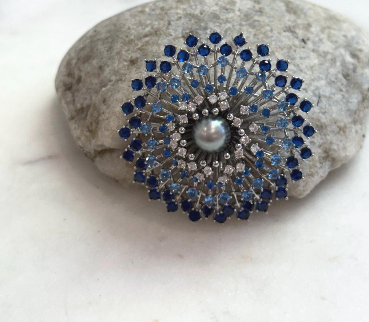 Firework-inspired pearl brooch pendant displayed against a natural stone.