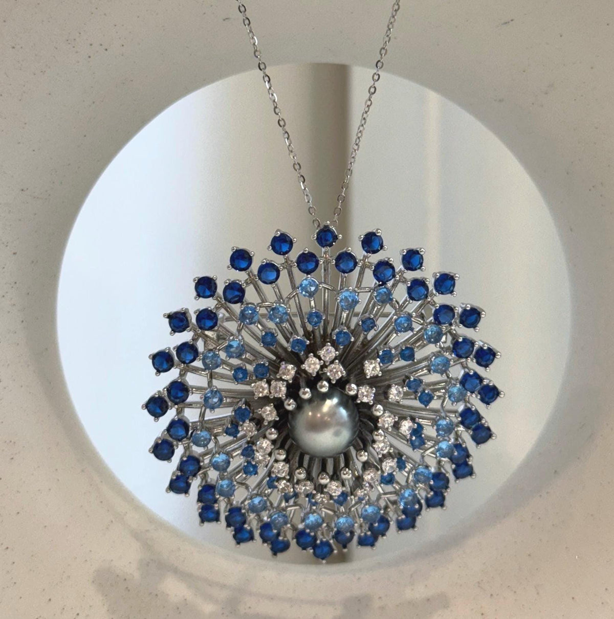 Blue stones arranged in radiating circles around a platinum gray Tahitian pearl.
