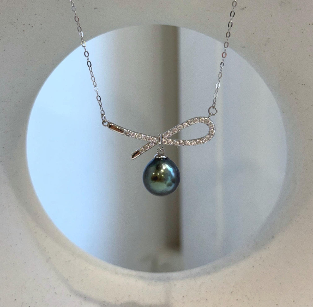 Reflective peacock green Tahitian pearl hanging from the center of a sterling silver bow.