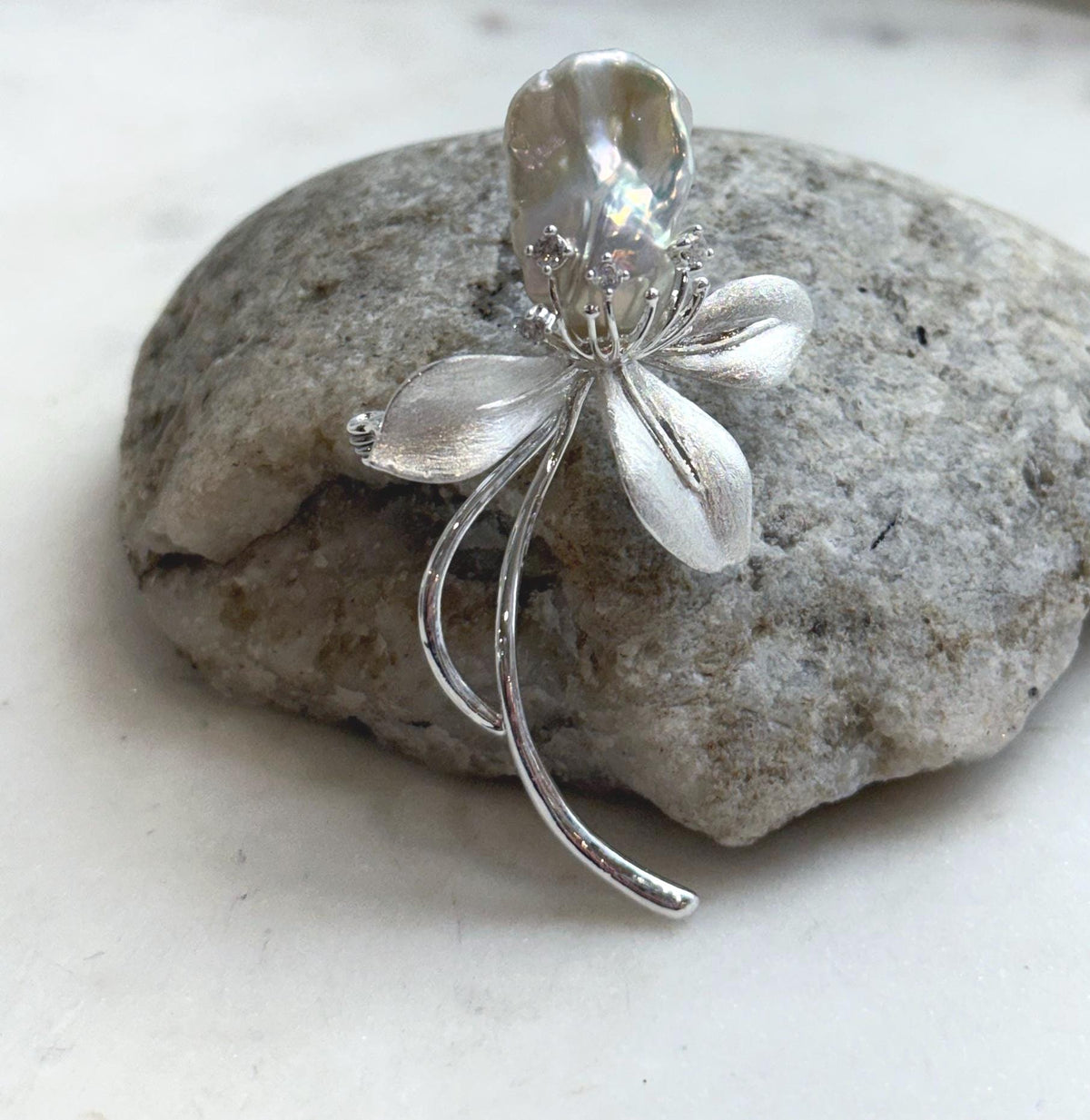 White baroque freshwater pearl brooch with a silver-tone floral design.