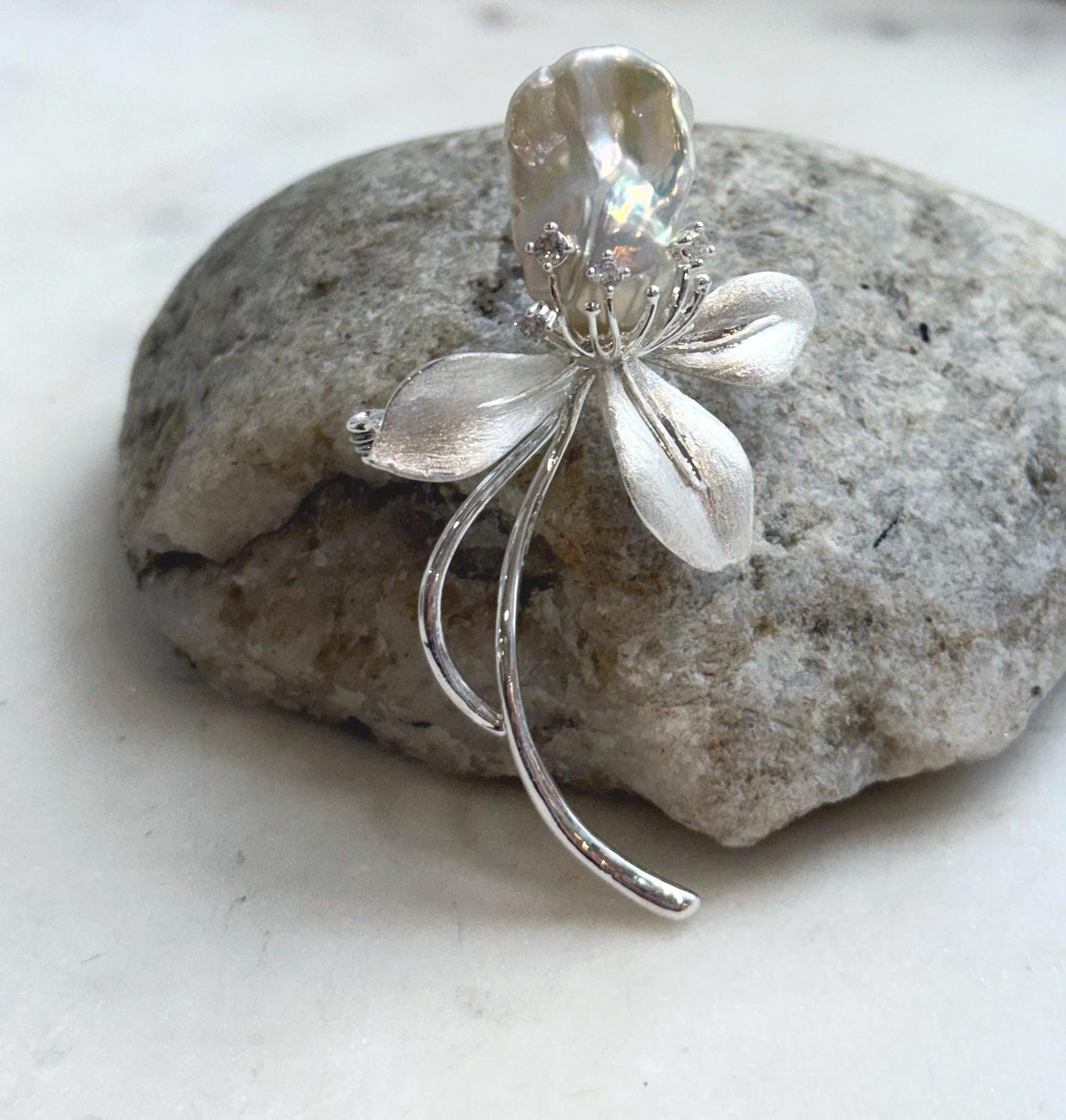 Floral pearl brooch displayed on a natural stone beside a window.