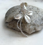 Floral pearl brooch displayed on a natural stone beside a window.