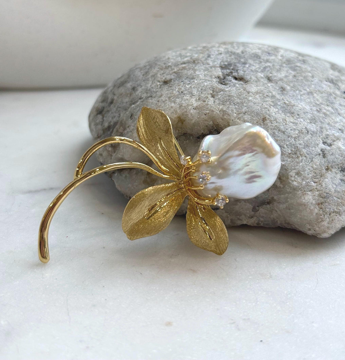 Floral pearl brooch with rainbow reflections and flowing gold-tone stems.