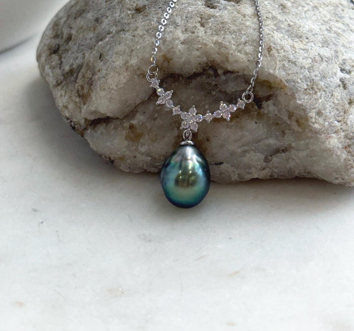 Teardrop Tahitian pearl pendant with mirror luster suspended from a curved row of sparkling silver flowers.